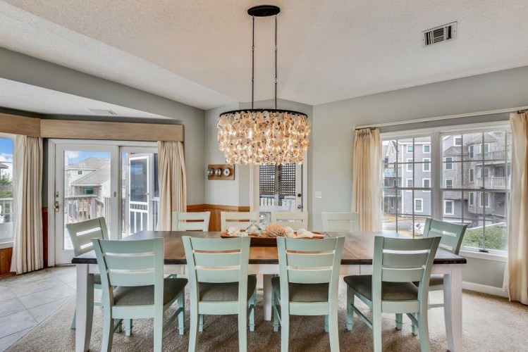 Gather around this inviting dining space where light floods through large windows, perfect for memorable meals together. The elegant chandelier and coastal-inspired chairs create a relaxed, welcoming atmosphere for your vacation dining.