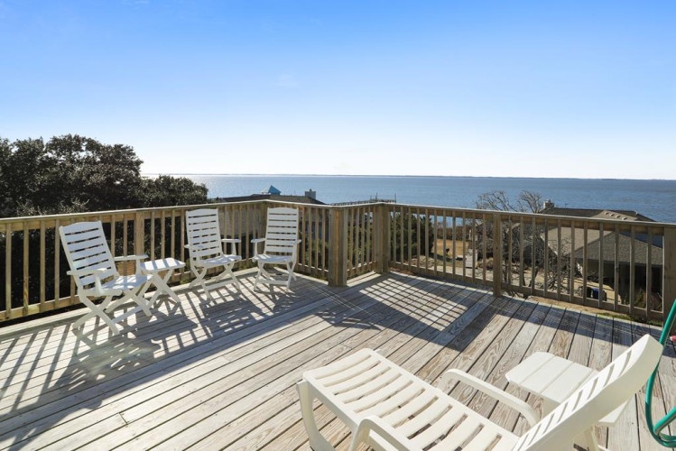An expansive deck overlooking the sparkling sea and lush coastal trees. Stretch out on the lounge chairs, soak up the sunshine, and let the ocean views wash over you in this peaceful seaside retreat.