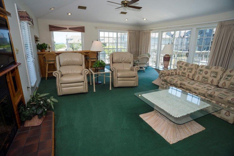 Relax in your spacious living room with plush recliners, a cozy sofa, and plenty of natural light streaming through large windows framing peaceful outdoor views.