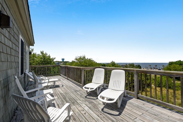 Soak up coastal sunshine on this private deck, where lounge chairs await your relaxation. Beyond the railing, lush greenery frames distant water views—perfect for morning coffee or sunset watching.