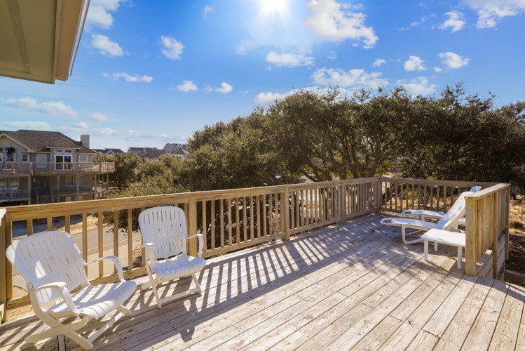 Spacious deck with lounge chairs overlooking mature trees and neighboring homes under a bright blue sky, perfect for morning coffee or sunset relaxation.