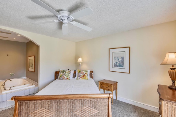 Your bright, airy bedroom awaits with a ceiling fan, plush bedding, and a soothing view into your private spa tub—perfect for unwinding after a day of adventure.