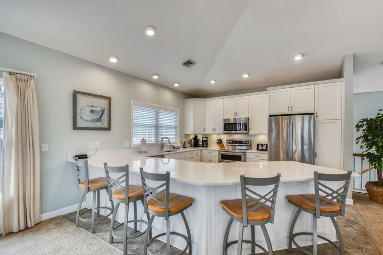 Your open-concept kitchen invites you to gather around the spacious island, where gleaming countertops and modern appliances make cooking a joy. Bright recessed lighting and soft coastal tones create a warm, welcoming space for your vacation memories.