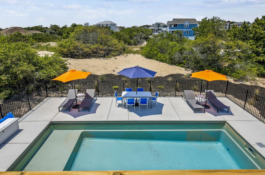 A spacious outdoor pool area surrounded by vibrant lounge seating and dining furniture provides the perfect spot for sun-soaked relaxation and al fresco meals with dune views beyond.