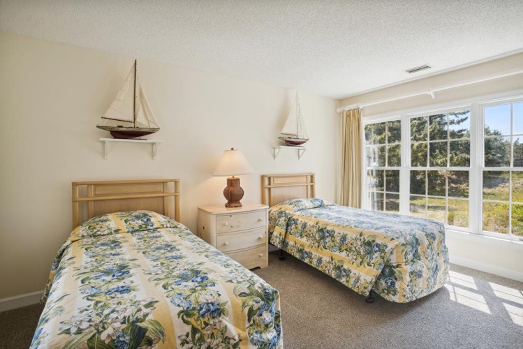 Your coastal retreat features twin beds dressed in fresh florals, model sailboats, and big windows framing lush greenery—inviting natural light and breezy relaxation.