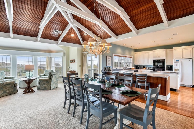Gather around the handcrafted dining table under soaring vaulted ceilings, where sunlight streams through expansive windows and the open-concept design invites effortless conversation from kitchen to living space.