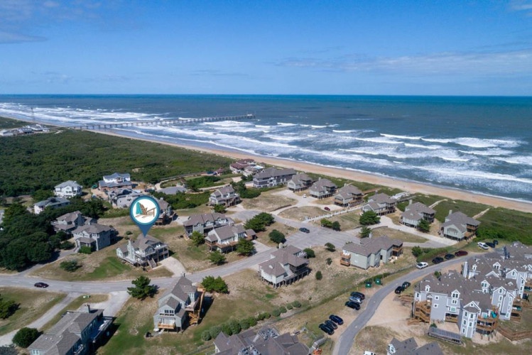 Aerial view of a beachfront residential community with the property located steps from the sandy shoreline and rolling ocean waves.