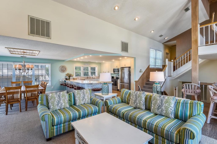 Step into your spacious open-plan living area with vaulted ceilings and coastal-inspired décor. Relax on comfy striped sofas, gather at the dining table, or explore the fully-equipped kitchen—your perfect home base for a memorable getaway.