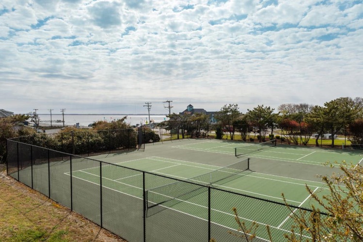 Tennis courts sit ready beneath a dramatic coastal sky, part of the property's recreational offerings and scenic surroundings near the water.