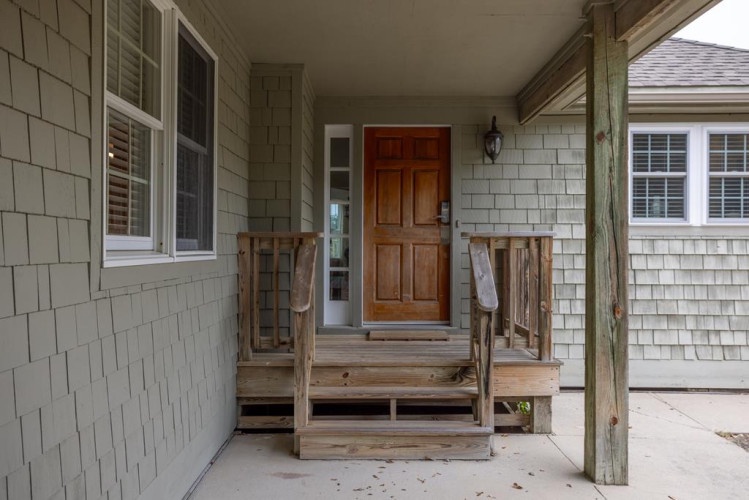 This charming entrance showcases classic coastal architecture with natural wood steps leading to a welcoming front door, perfect for your arrival at this peaceful retreat.
