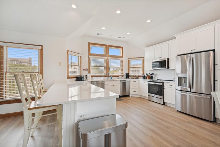 Step into your bright, open kitchen where white cabinetry meets stainless steel appliances and abundant natural light pours through wood-trimmed windows—perfect for preparing family meals or morning coffee.