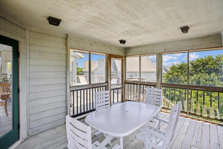 A covered screened porch offers comfortable seating for outdoor dining with treetop views and coastal breezes, perfect for morning coffee or evening meals in the fresh air.