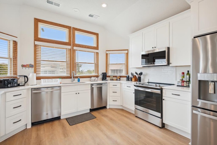 Cook your favorite meals in this bright, fully equipped kitchen with stainless steel appliances, sleek white cabinetry, and natural light streaming through elegant wood-framed windows.