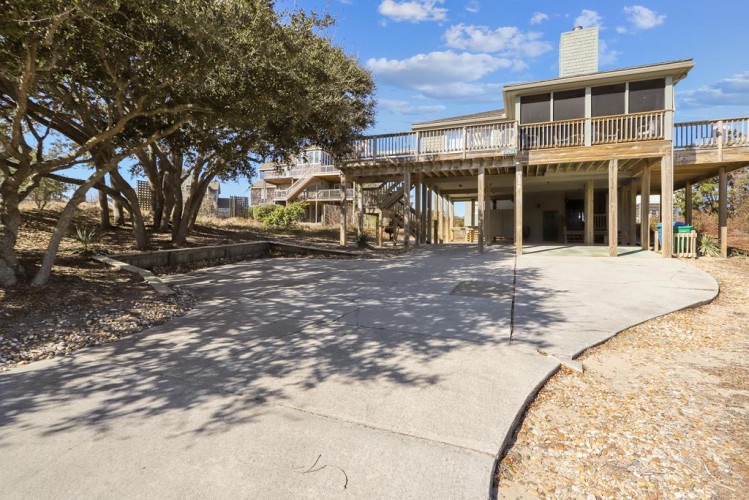 Elevated beach home with scenic landscaping and multi-level deck spaces, offering convenient covered parking and a welcoming coastal retreat atmosphere.