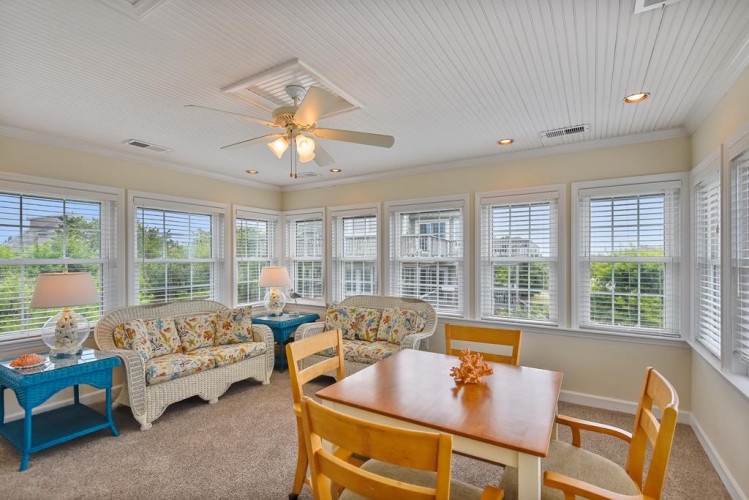 Settle into this bright, airy sunroom where natural light pours through wrap-around windows. Relax on wicker sofas or gather at the wooden dining table for meals with garden views all around.