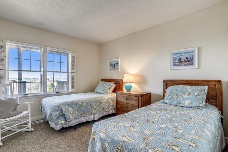 Relax in your coastal bedroom with twin beds dressed in soft blue bedding and peaceful ocean views just beyond your windows. Natural light fills the space, welcoming you to unwind.