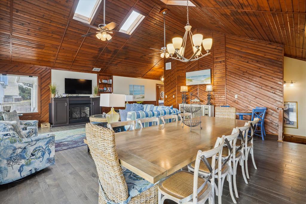 Step into your coastal retreat where soaring wood-paneled ceilings meet cozy comfort. Gather around the dining table for meals or relax by the fireplace, all bathed in natural skylight glow.