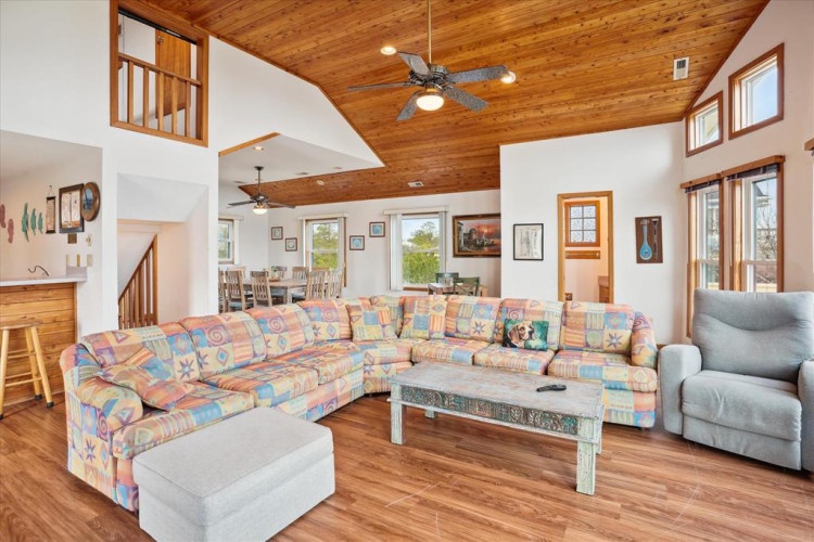 Relax in your spacious living room with vaulted wood ceilings, ceiling fans, and natural light streaming through large windows. The open layout flows into dining and kitchen areas, perfect for gathering.