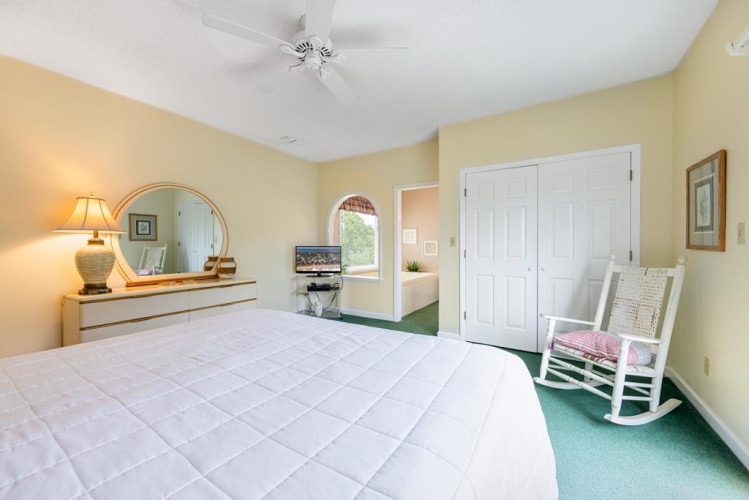 Relax in your spacious retreat with a plush bed, calming yellow walls, and a gentle ceiling fan overhead. A cozy rocking chair invites you to unwind by the window.