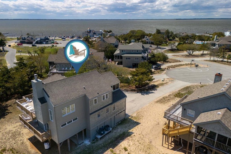 Aerial view of a waterfront coastal neighborhood with bay access, beach proximity, and charming residential homes nestled among mature trees.