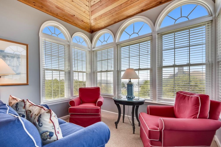 Your bright living space features stunning arched windows and a vaulted wood ceiling, creating an airy retreat where you can relax in cozy seating while enjoying natural light.