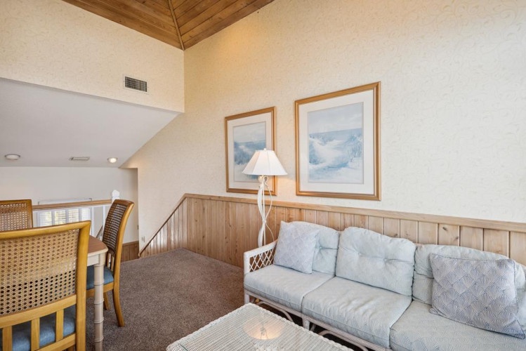 Step into your inviting loft living space with vaulted wood ceilings, a cozy seating area, and coastal artwork creating a relaxing retreat atmosphere.