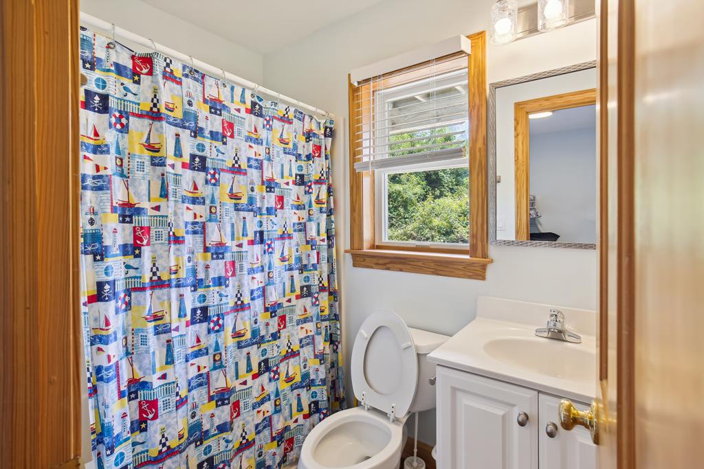 Your bright bathroom features a coastal-themed design, with a playful nautical shower curtain, white vanity, and a window offering natural light and garden views.