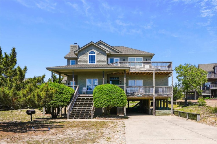 This coastal vacation home features multiple covered porches and a welcoming elevated design, set among coastal landscaping in a peaceful residential area.