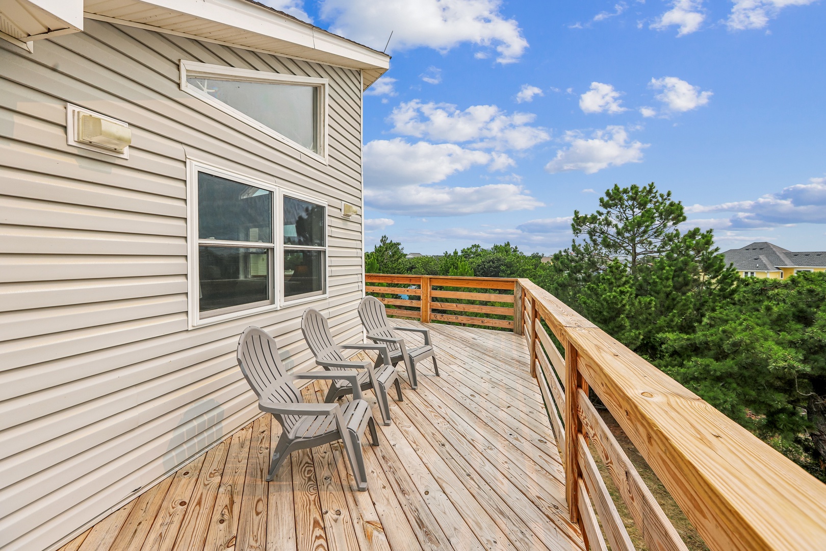 The spacious upper-level deck features two Adirondack chairs and overlooks lush greenery and neighboring rooftops under open skies—a serene spot for your morning coffee or evening relaxation.