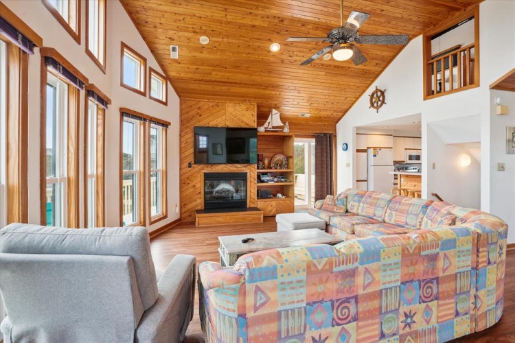 Relax in your spacious living room with vaulted wood ceilings, cozy fireplace, and abundant natural light streaming through floor-to-ceiling windows. Unwind on plush sofas as you enjoy your favorite shows or simply soak in the warm, nautical-inspired ambi