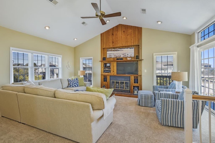 You'll love gathering in this bright, vaulted living room, where natural light pours through large windows, plush seating invites relaxation, and a cozy fireplace warms up your evenings together.