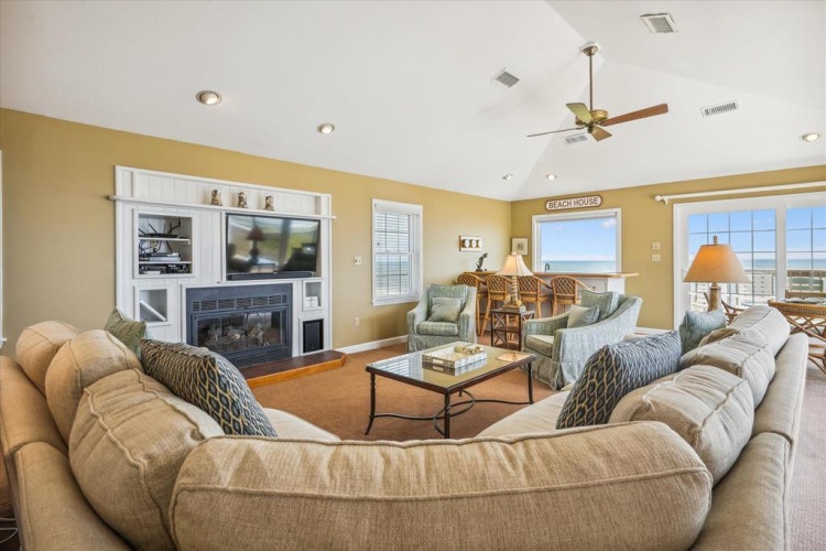 Picture yourself relaxing in this inviting living room, where plush seating surrounds a cozy fireplace and ocean breezes drift through the windows—your perfect beach retreat.