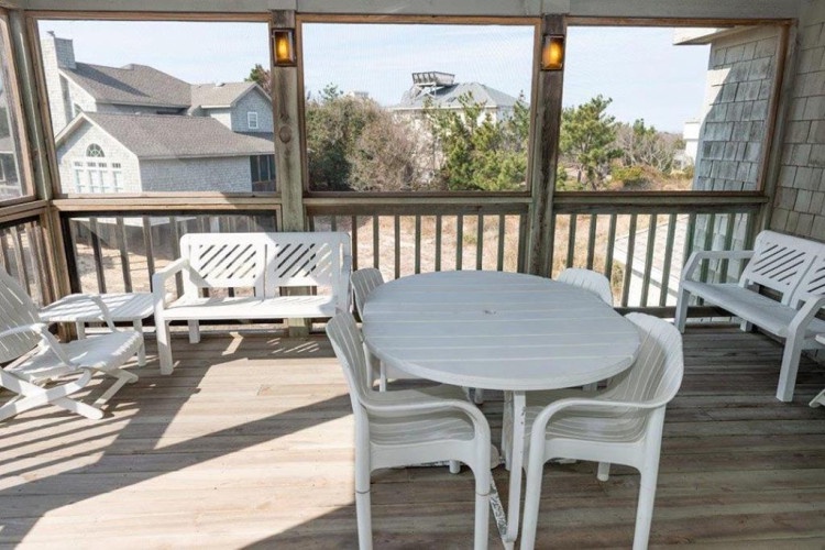 A screened porch overlooking a residential neighborhood, offering a shaded space to dine and unwind outdoors while staying protected from insects.