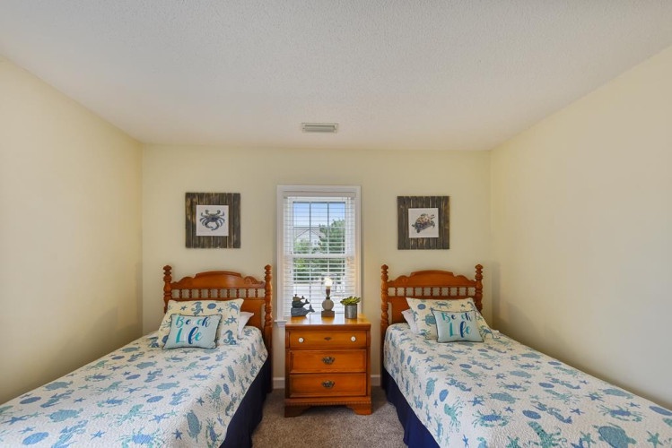 Unwind in your cozy bedroom with twin beds adorned in cheerful coastal linens, where restful mornings begin with natural light streaming through the window.