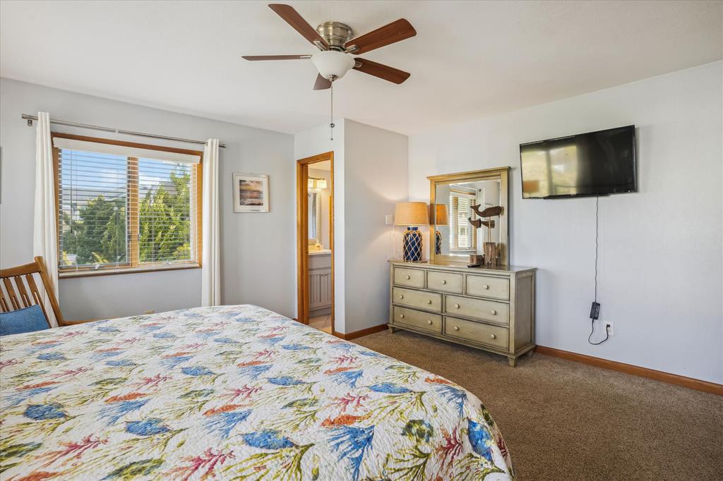 Unwind in your bright, airy bedroom with a cozy bed, ceiling fan, TV for entertainment, and a view of lush greenery through the window.