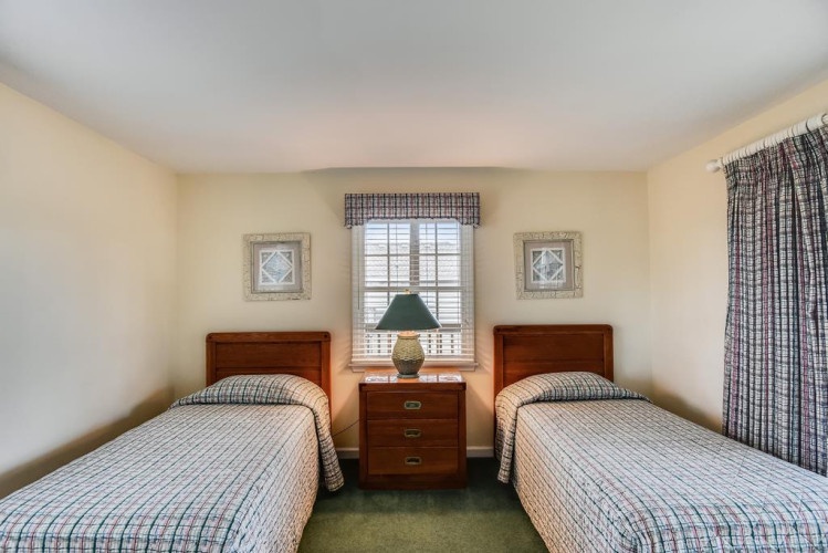 A peaceful twin bedroom awaits you with matching wood furnishings, cheerful plaid linens, and soft natural light—perfect for family or friends sharing your getaway.
