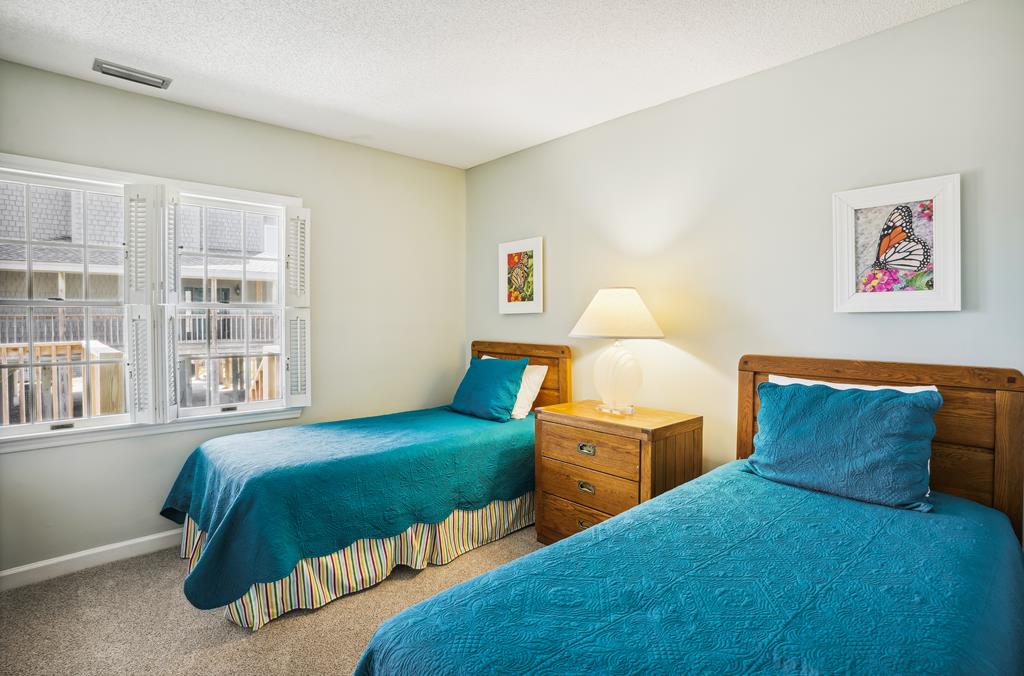 Your restful retreat awaits with two cozy twin beds dressed in vibrant turquoise linens, a warm bedside lamp for evening reading, and cheerful butterfly art that brightens your space.