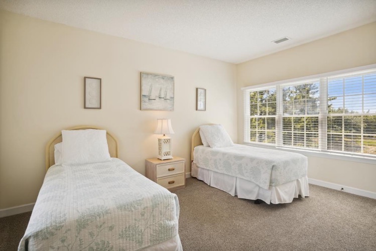 Two cozy twin beds await you in this serene bedroom, where soft natural light pours through the large windows, creating a peaceful retreat for restful sleep.
