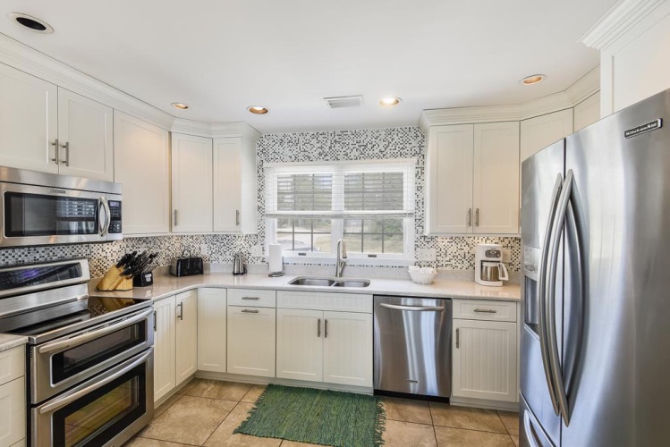 Prepare your favorite meals in this bright, fully-equipped kitchen featuring stainless steel appliances, ample counter space, and cheerful natural light from the window above the sink.