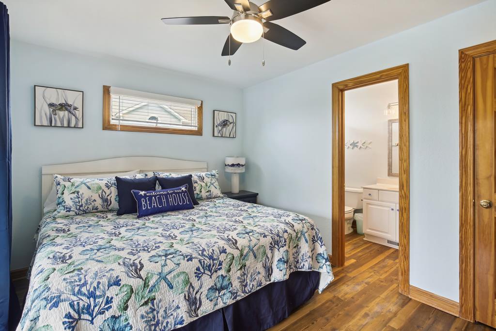 Settle into your coastal retreat where calming blues meet crisp whites. The ceiling fan keeps you cool while natural light streams in, highlighting charming botanical artwork and a welcoming bed dressed in beach-inspired linens.