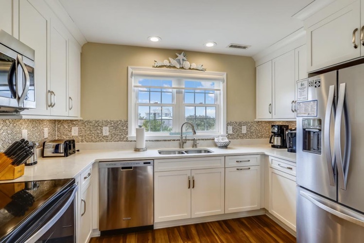 Your beautifully appointed kitchen features white cabinetry, stainless appliances, and a window with natural light overlooking the area. Perfect for preparing memorable meals during your stay.