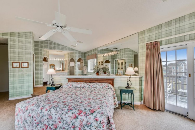 You'll love the spacious comfort of this beautifully appointed bedroom, featuring elegant plaid wallpaper, ceiling fan, walk-in closets, private balcony access, and bedside tables for your convenience.