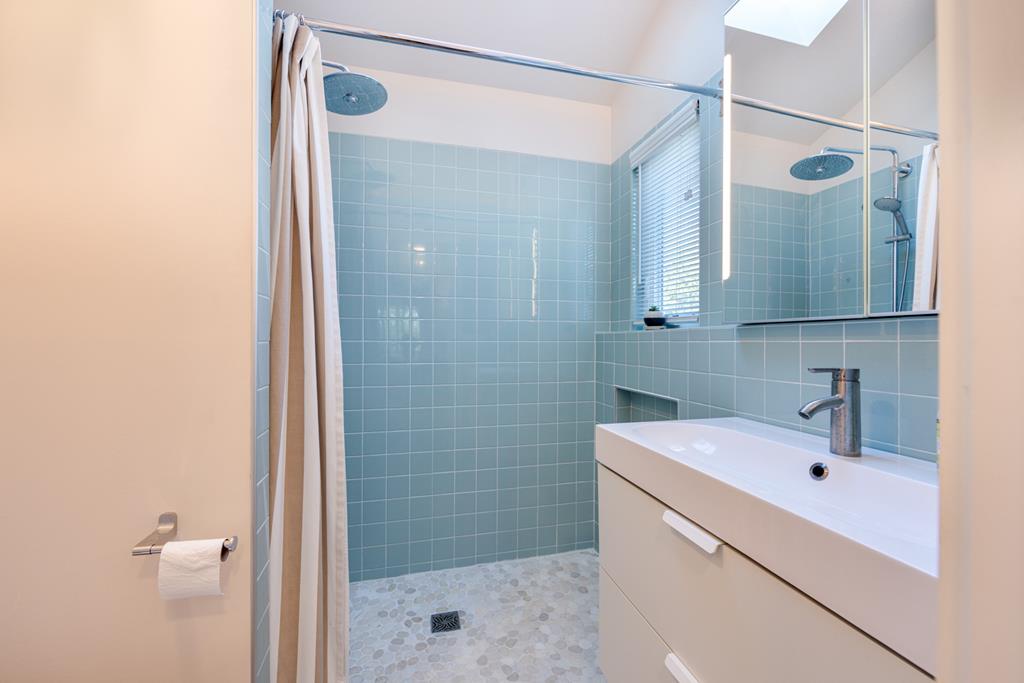 Step into your bright, modern bathroom featuring calming blue tiles, a spacious walk-in shower with rainfall showerhead, and a sleek vanity—your private retreat after exploring.