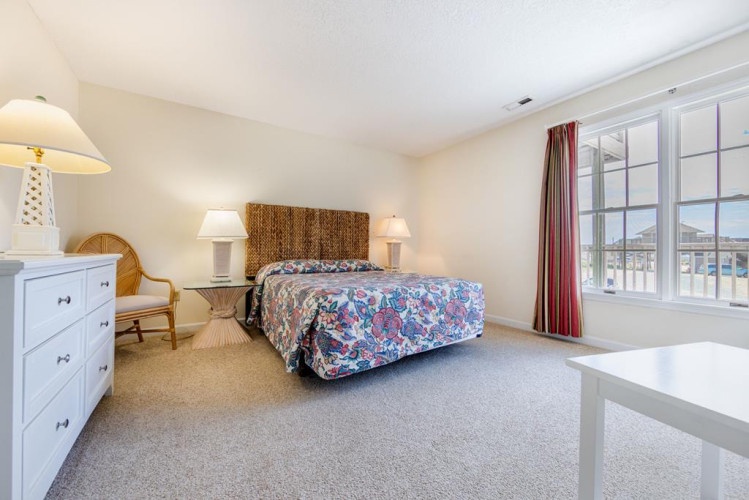 Unwind in your bright, coastal-style bedroom where natural light streams through large windows. The woven headboard and floral bedding set a relaxed beach-house tone for restful nights.