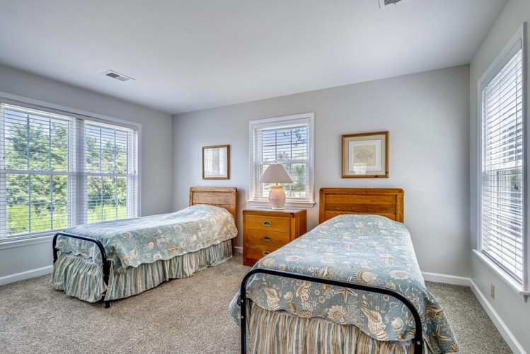 Two comfortable beds await in this bright, peaceful bedroom. Natural light fills the space, while soft blue linens and classic wood furnishings create a restful retreat for your stay.
