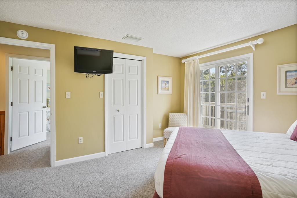Settle into your bright, sunlit bedroom where large windows invite views of nature and natural light, while a cozy armchair and mounted TV offer the perfect retreat after your day's adventures.