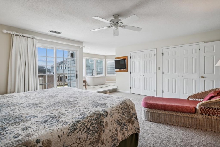 Your spacious retreat features a plush bed, ceiling fan, bright natural light, flat-screen TV, and a sliding door leading to your private balcony with glimpses of nearby homes.