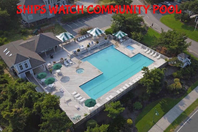 Aerial view of the Ships Watch Community Pool, featuring a large swimming pool, multiple umbrellas, lounge seating, and a small spa surrounded by trees and nearby residential buildings.