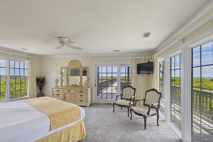 Your spacious suite opens to breathtaking treetop and ocean views from floor-to-ceiling windows, where sunlight bathes the cozy seating area and plush bed—your perfect coastal escape.
