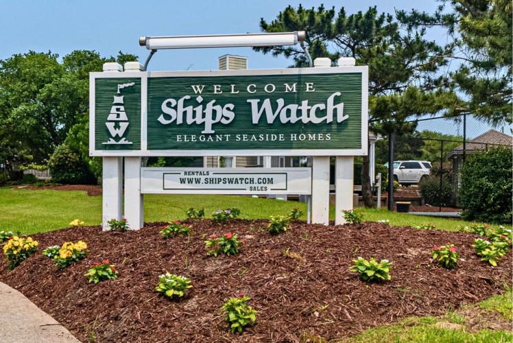 Welcome to Ships Watch, an elegant seaside property surrounded by lush coastal landscaping. The property entrance features a classic nautical charm with inviting greenery and mature pines.